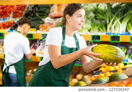 Friendly female vendor laying out ripe melon on counter 127338347