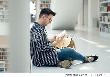 Man, student and reading in library with book for knowledge, education or learning at the university. Male learner in study with books for thesis, project or assignment for scholarship at the campus 127339130