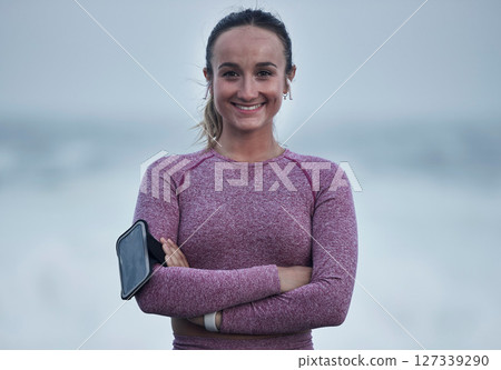 Portrait, runner and woman with arm band, music earphones and motivation for cardio fitness in Sweden. Happy young athlete, arms crossed and training for healthy lifestyle, energy and sports wellness 127339290