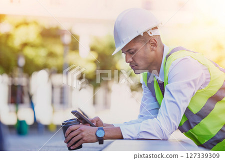Construction engineer, man and coffee with phone for typing, reading notification or architect management in city. Industrial contractor, smartphone and coffee break for online mobile tech connection 127339309