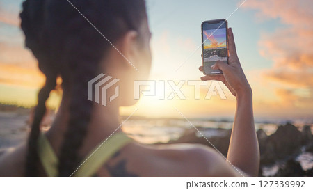 Beach, phone and woman taking photo of sunset for social media during evening workout in Bali. Nature, ocean and fitness influencer with picture of sun in blue sky on smartphone screen in Indonesia. Beach, phone and woman taking photo of sunset for social media during evening workout in Bali. Nature, ocean and fitness influencer with picture of sun in blue sky on smartphone screen in Indonesia. 127339992
