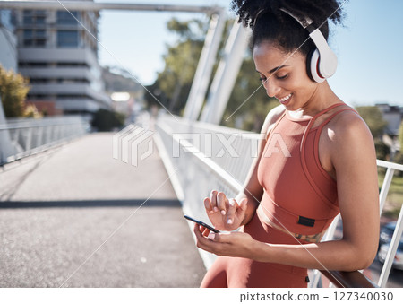 Fitness, headphones and black woman with phone in city for social media or texting. Sports, exercise and happy female on break streaming music, radio or podcast on 5g mobile smartphone after training 127340030