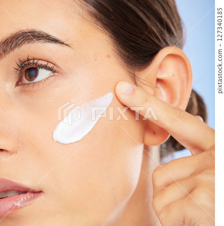 Face, beauty skincare and woman with cream in studio isolated on a blue background. Thinking, cosmetics and female model apply facial lotion, creme and moisturizer product for healthy skin hydration. Face, beauty skincare and woman with cream in studio isolated on a blue background. Thinking, cosmetics and female model apply facial lotion, creme and moisturizer product for healthy skin hydration. 127340185