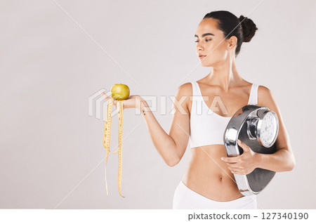 Fitness, health and woman with scale and apple for weightloss, diet and nutrition on white studio background. Exercise, wellness and girl with fruit, balance and measuring tape for healthy lifestyle Fitness, health and woman with scale and apple for weightloss, diet and nutrition on white studio background. Exercise, wellness and girl with fruit, balance and measuring tape for healthy lifestyle 127340190