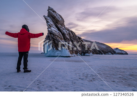 Tourist standing in front of the Dragon tail rock before sunrise. It's located at Ogoy island in frozen lake Baikal, Russia. 127340526