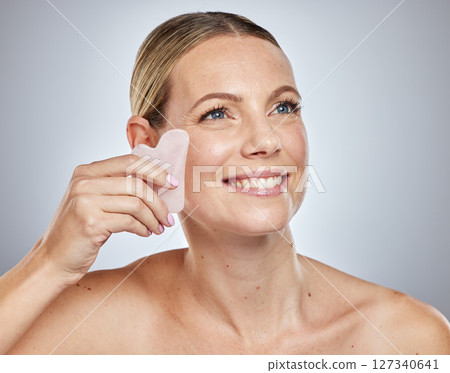Face, beauty skincare and woman with crystal isolated on a gray studio background. Thinking, health and female model with rose quartz stone or guasha product for anti aging, massage and healthy skin. 127340641
