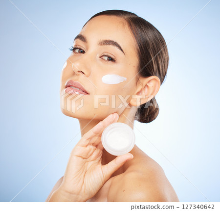 Woman, face and cream for skincare beauty, salon spa wellness and cosmetics dermatology in blue background. Model, relax facial care and mouisturizer morning routine in studio with luxury product 127340642
