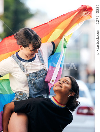 Women, lgbtq couple and piggyback with flag for pride, love and support in city street. Diversity, lesbian and gay friends celebrate rainbow identity, freedom and happiness of human rights together 127340825