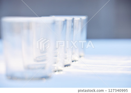 Glass, crockery and mockup with a row of drinking glasses on a table in a studio or restaurant for fine dining. Space, glassware and drinks with a group of cups in a line for a beverage while dining Glass, crockery and mockup with a row of drinking glasses on a table in a studio or restaurant for fine dining. Space, glassware and drinks with a group of cups in a line for a beverage while dining 127340995