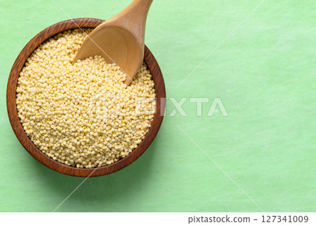 Yellow millet grain in wooden bowl with spoon on green background, Food ingredient, Top view Yellow millet grain in wooden bowl with spoon on green background, Food ingredient, Top view 127341009