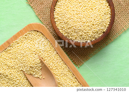 Yellow millet grain in wooden bowl and plate on green background, Food ingredient, Top view Yellow millet grain in wooden bowl and plate on green background, Food ingredient, Top view 127341010