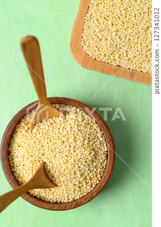 Yellow millet grain in wooden bowl with spoon on green background, Food ingredient 127341012
