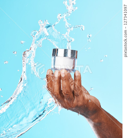 Hand, water splash and black man with cream for skincare in studio on a blue background. Cosmetics, hygiene and male model holding lotion, creme or moisturizer product for healthy skin and beauty. Hand, water splash and black man with cream for skincare in studio on a blue background. Cosmetics, hygiene and male model holding lotion, creme or moisturizer product for healthy skin and beauty. 127341097