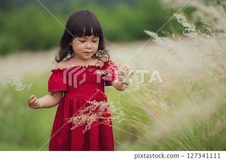 toddler girl in red dress playing grass flower in field 127341111