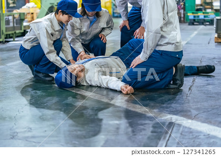 A group of people providing medical assistance to a worker who collapsed at a factory A group of people providing medical assistance to a worker who collapsed at a factory 127341265