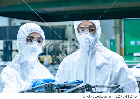 Male and female workers wearing protective clothing working in a factory 127341270