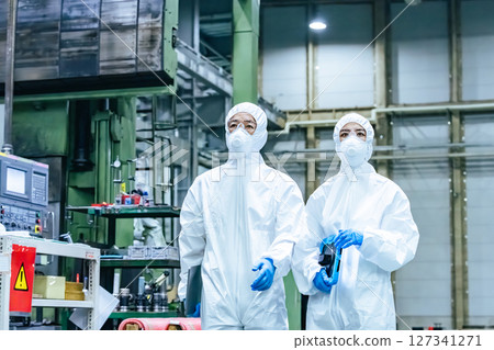 Male and female workers in protective clothing walking through a factory Male and female workers in protective clothing walking through a factory 127341271