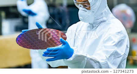 A male worker in a dustproof suit inspecting silicon wafers in a semiconductor factory A male worker in a dustproof suit inspecting silicon wafers in a semiconductor factory 127341273