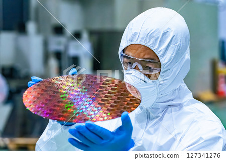 Male worker in protective clothing inspecting silicon wafers in a semiconductor factory Male worker in protective clothing inspecting silicon wafers in a semiconductor factory 127341276