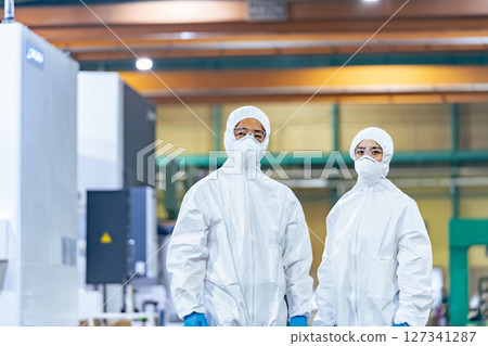 Male and female workers wearing protective clothing standing in a factory 127341287