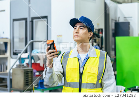 A worker using a portable measuring device in a factory A worker using a portable measuring device in a factory 127341288