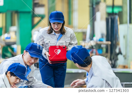 A group of people using an AED to help a worker who collapsed at a factory A group of people using an AED to help a worker who collapsed at a factory 127341303