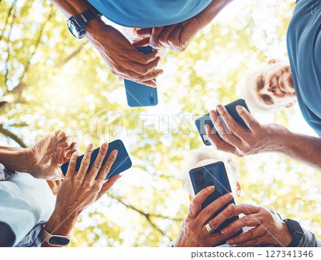 Fitness, group with smartphone in hands and running in park, technology low angle and check exercise mobile app. Elderly runner team outdoor with health, phone for cardio and sports motivation. Fitness, group with smartphone in hands and running in park, technology low angle and check exercise mobile app. Elderly runner team outdoor with health, phone for cardio and sports motivation. 127341346