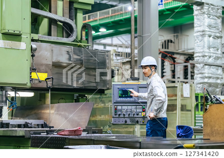 A male worker operates a machine on a control panel in a factory 127341420