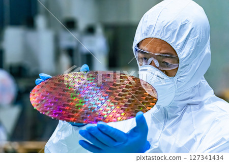 Male worker in protective clothing inspecting silicon wafers in a semiconductor factory 127341434