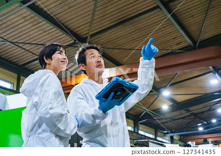 Male and female workers in protective clothing inspecting a factory 127341435