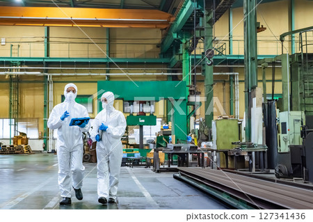 Male and female workers wearing protective clothing walking through a factory 127341436