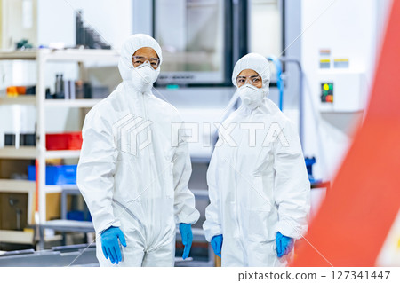 Male and female workers wearing protective clothing standing in a factory 127341447