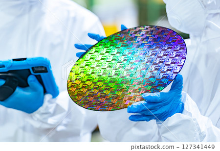 Male and female workers in protective clothing holding tablets and inspecting silicon wafers in a semiconductor factory 127341449