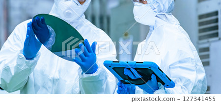 A male worker in a dustproof suit inspecting silicon wafers in a semiconductor factory A male worker in a dustproof suit inspecting silicon wafers in a semiconductor factory 127341455