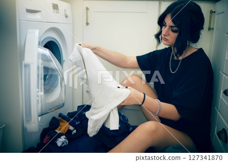 Laundry, cleaning and housework with a woman using the washing machine in her home for domestic responsbility. Appliance, fabric and clothes with a female cleaner on her apartment floor to wash 127341870