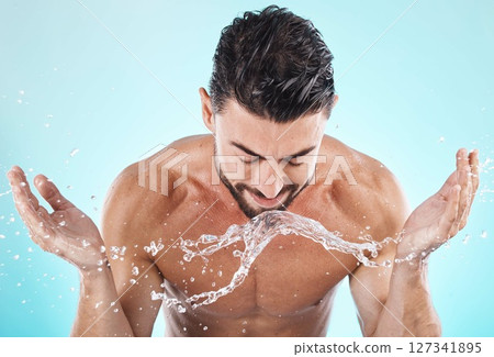 Skincare, water splash and man in a studio for a wellness, health and self care body routine. Cosmetics, hydration and male model with natural dermatology facial treatment isolated by blue background Skincare, water splash and man in a studio for a wellness, health and self care body routine. Cosmetics, hydration and male model with natural dermatology facial treatment isolated by blue background 127341895