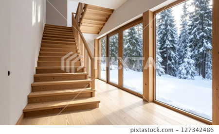 Modern house interior featuring an empty, contemporary wooden staircase with glass railings, leading up through a bright, sunlit hall 127342486