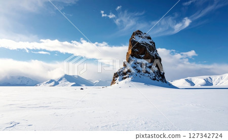 Majestic Mountain Peak in Icy Wilderness: An awe-inspiring view of a mountain peak rising dramatically from a vast, icy expanse beneath a serene, cloud-dappled sky. 127342724