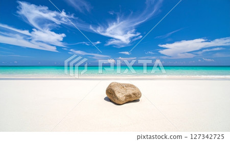 Tranquil Stone on Pristine Shore: A single, weathered stone rests serenely upon an immaculate sandy beach. Crystal-clear turquoise waters meet an azure sky dotted with wispy clouds. 127342725
