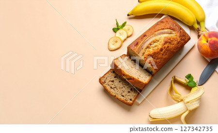Banana Bread Delight: Slices of moist banana bread, adorned with banana slices and a peach, rest on a light beige surface, ready to be savored. A perfect image for food blogs and culinary websites. 127342735