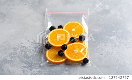 Fresh Fruit Sealed: A vibrant arrangement of juicy orange slices and plump blackberries, artfully enclosed within a transparent, sealed bag, ready for a delightful treat. 127342737