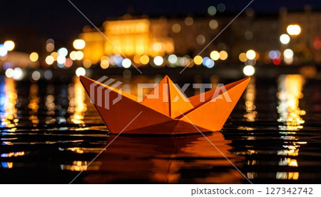 Nighttime Paper Boat: An orange paper boat floats serenely on dark water, reflecting city lights in the background. 127342742