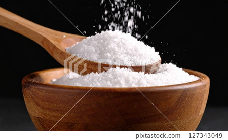 Wooden spoon pouring salt into bowl on black background 127343049