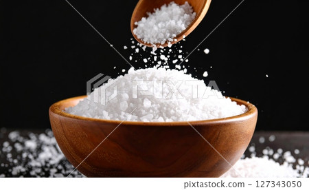 Wooden spoon pouring salt into bowl on black background 127343050