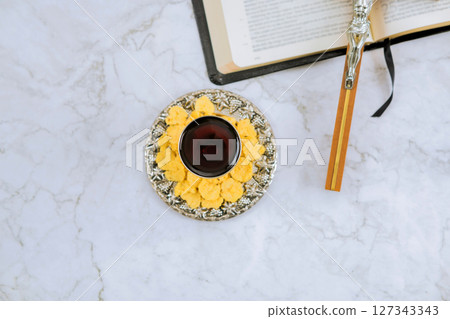 Wine beverage rests on decorative plate next to an open Holy Bible, wooden cross peaceful atmosphere in church 127343343