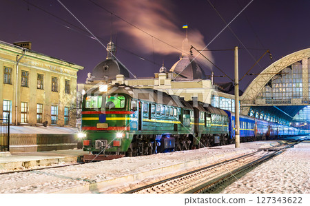 Green diesel locomotive waits with a passenger train beside snow-covered tracks at Lviv's historic main railway station in Ukraine 127343622