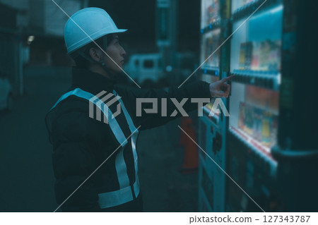 A security guard on a break buying a drink from a vending machine A security guard on a break buying a drink from a vending machine 127343787