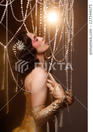 Retro-style performer in vintage costume posing on dark stage under chandelier 127344075