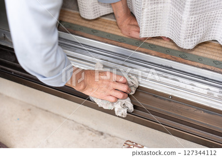 A senior woman cleaning the aluminum sash slats with a rag 127344112