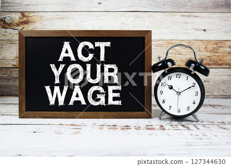 Act Your Wage text message and alarm clock on wooden background Act Your Wage text message and alarm clock on wooden background 127344630